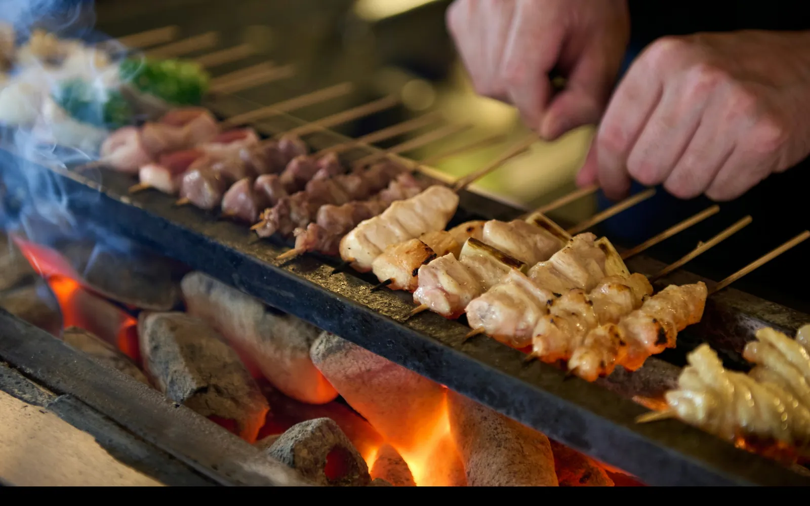 備長炭の焼き台で串を焼いている手元。炭の粒と炎が見える