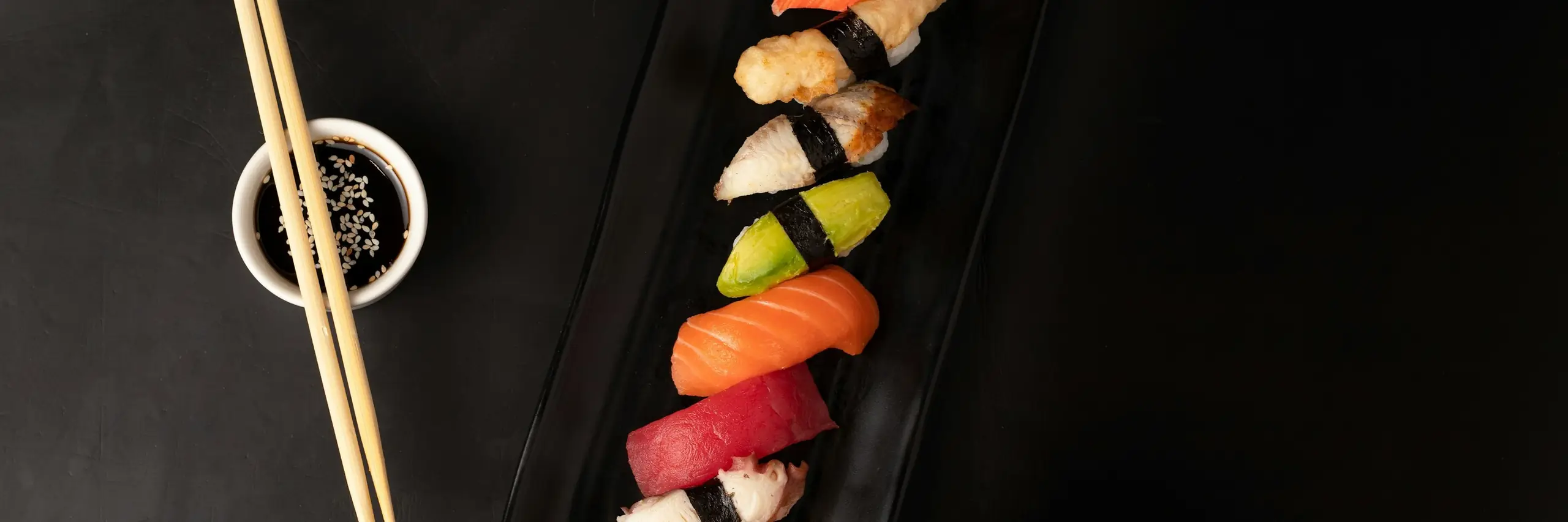 黒い長皿に並んだ握り寿司。醤油皿と箸が添えてある